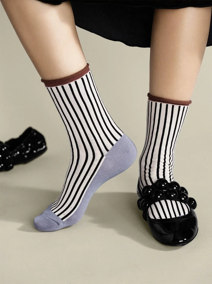 Hilda Crew socks in Pebble — worn on feet with black bubble-strap flats, showing black and white stripe body, brown rolled cuff, and grey sole