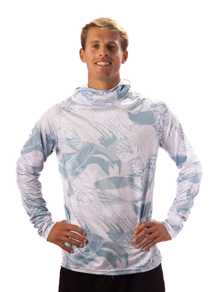 Male model wearing the Waihana Island Sky Fishbone long-sleeve hooded sun shirt in light blue and white fish-print pattern, hands on hips against a white studio background.
