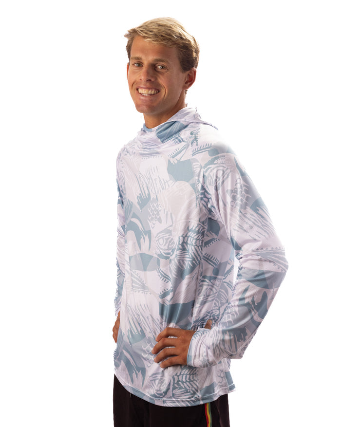 Smiling male model wearing the Waihana Island Sky Fishbone hooded sun shirt with long sleeves and an all-over light blue and white fish-print pattern, shown from a side angle against a white background.