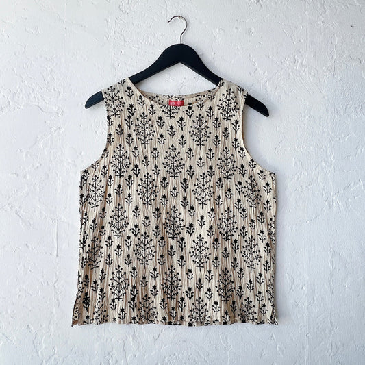 Beige sleeveless top with black floral pattern on a hanger against a white wall
