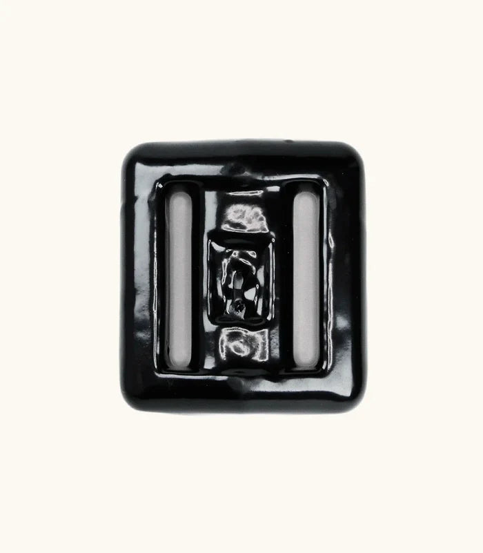 Black rubber-coated lava rock dive weight with two strap slots, photographed from above on a light background.