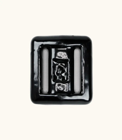 Black rubber-coated lava rock dive weight with two strap slots, photographed from above on a light background.