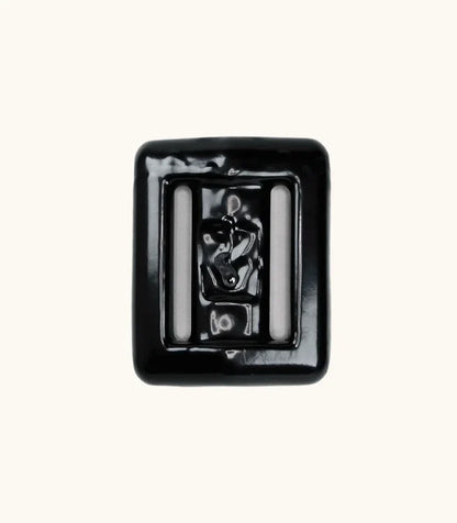 Close-up of a single black lava rock dive weight with glossy coating and two integrated belt slots, shown against a clean off-white background.