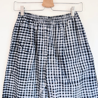Close-up of the waistband and upper leg of the Lazy Pants in Indigo Gingham, showing the elastic waistband, side pocket opening, and hand-printed black and white gingham check pattern with natural Batiki dye variation