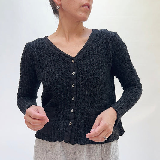 Person wearing a black textured cardigan against a plain background
