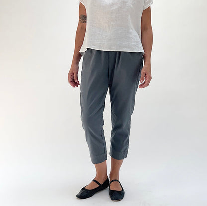 Full front view of model wearing Cut Loose linen-Tencel crop pant in iron, showing charcoal grey color, elastic waist, and tapered leg narrowing at the ankle
