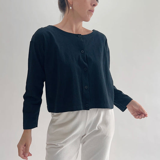Three-quarter front view of model wearing Pacific Cotton black long sleeve button front shirt, showing wide scoop neckline, five-button center placket, long sleeves, boxy cropped fit, and black color
