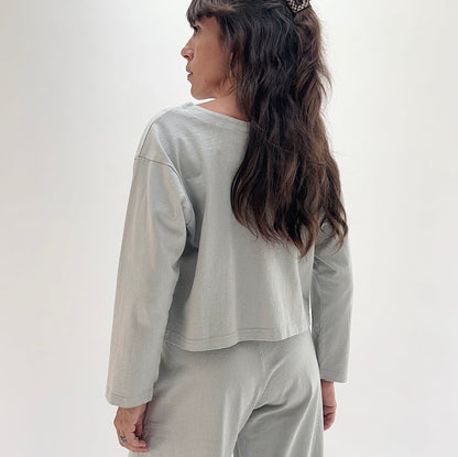 Back view of model wearing Pacific Cotton orlaya long sleeve button front shirt, showing relaxed cropped boxy silhouette, long sleeves, and straight hem