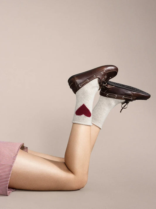 Person wearing white socks with a red heart design and brown shoes on a beige background