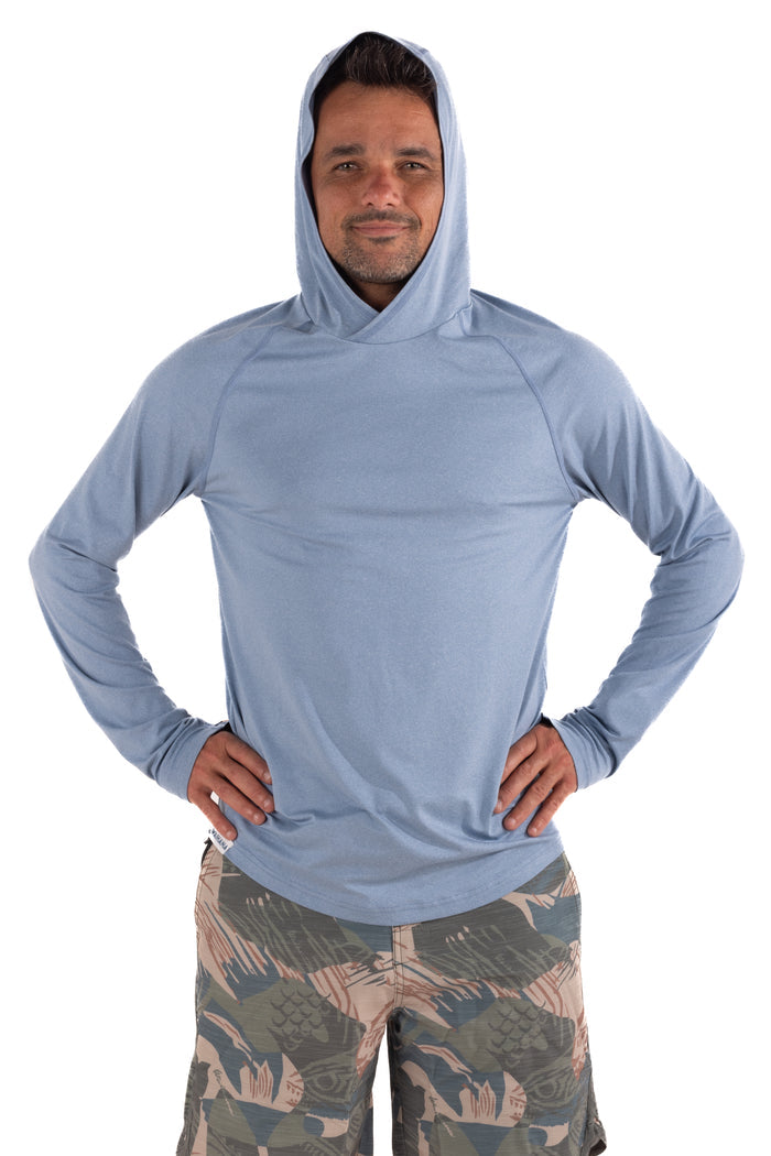 Man wearing the Waihana Mariner Blue Hooded Long Sleeve Sun Shirt with camo board shorts, hands on hips, front view on white background.