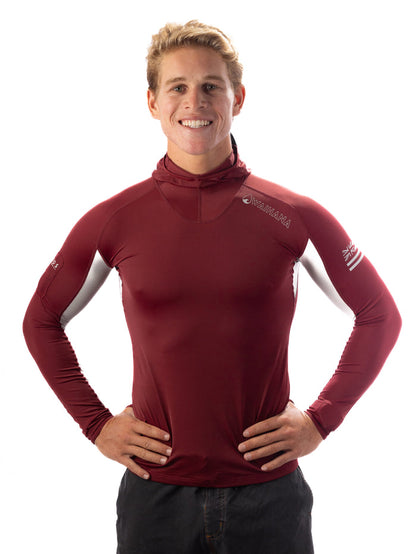 Smiling male model wearing a maroon Waihana Carvico hooded surf rashguard with white side panels and Hawaiian flag sleeve detail, hands on hips against a white background.