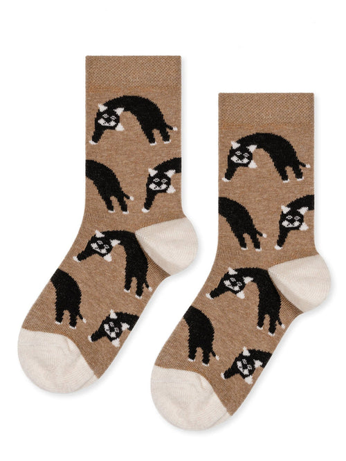 A pair of beige socks with a pattern of black cats in various poses.
