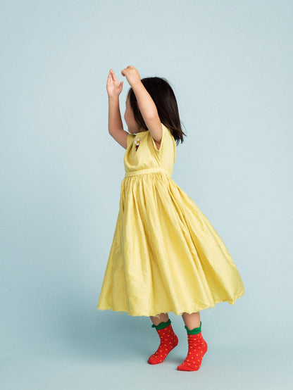 Child in a yellow dress and red, yellow and green socks designed to resemble strawberries standing against a blue background