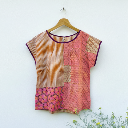Colorful patterned red, orange and pink top on a wooden hanger against a white background