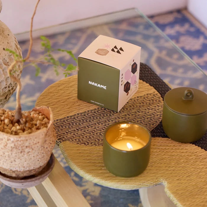 Small table with a potted plant, candle, and box labeled 'Nakame' on a patterned rug.