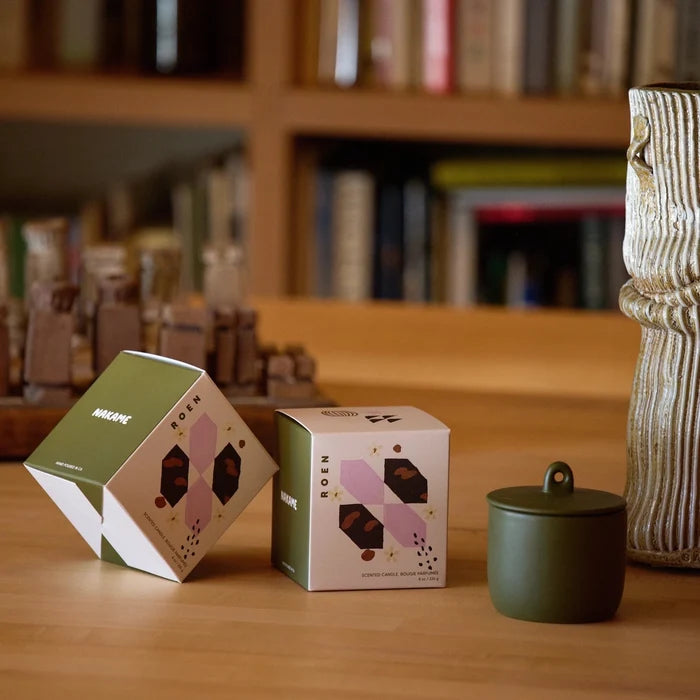 Two boxes with a design on a wooden surface, with a blurred bookshelf in the background.