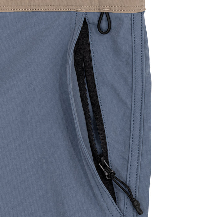Close-up of the zippered side pocket on Waihana's Offshore Blue Cruiser Shorts, featuring a black zipper with cord pull against slate blue fabric and a tan elastic waistband.