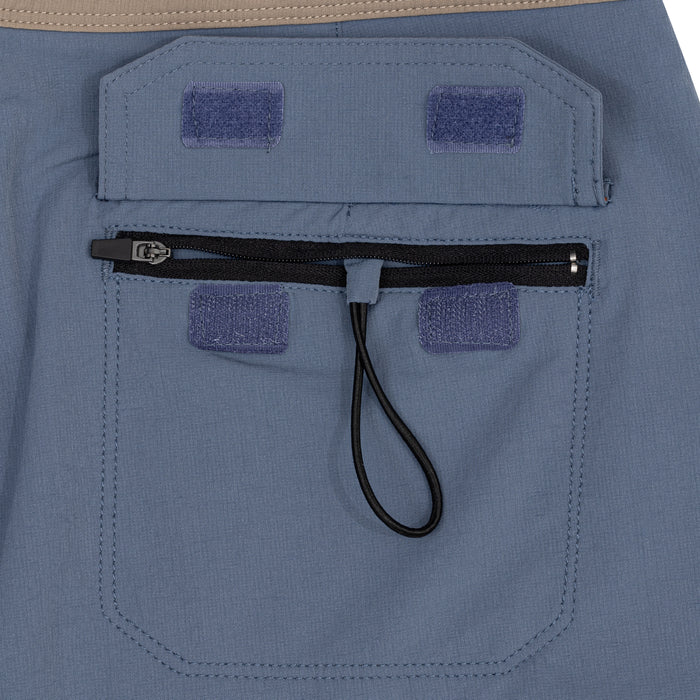 Close-up of the back zippered pocket on the Waihana Offshore Blue Cruiser board shorts, featuring velcro patches on both the flap and pocket, a black zipper with bungee pull tab, and slate-blue ripstop fabric.