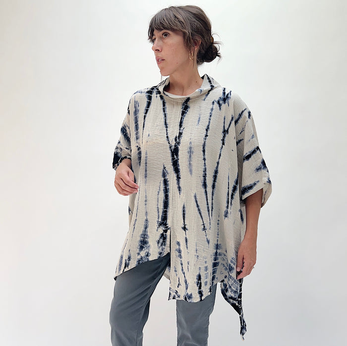 Model wearing the Eleven Stitch one size asymmetrical travel pullover in indigo tie-dye, three-quarter front view showing draped silhouette and asymmetrical hem