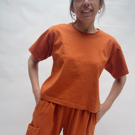 Person wearing an orange t-shirt and pants against a plain background