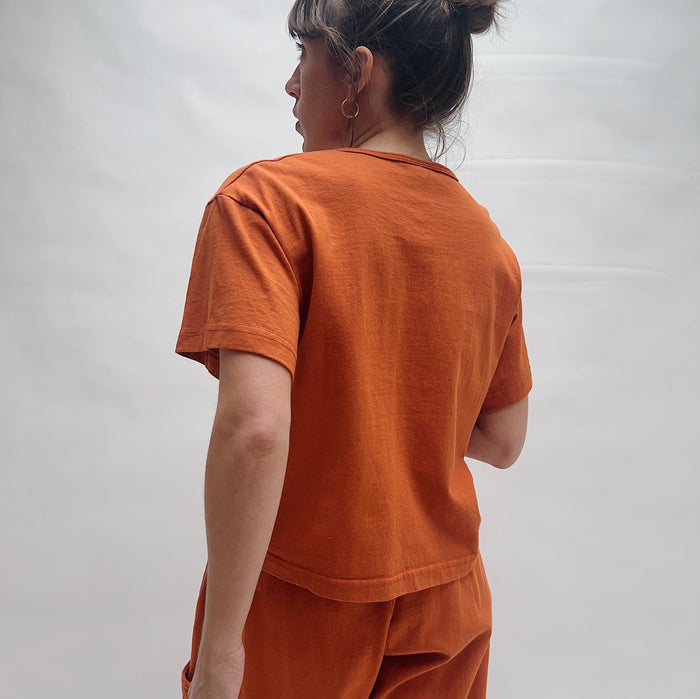 Person wearing an orange t-shirt and pants against a white background, viewed from the back