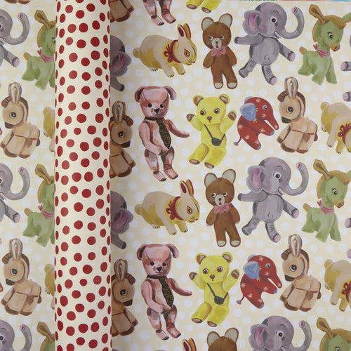 Plushies wrapping paper by Nathalie Lété shown rolled and flat, displaying vintage-style illustrated plush animals including teddy bears, elephants, rabbits, and donkeys on a cream background, with the red polka dot reverse visible on the rolled tube