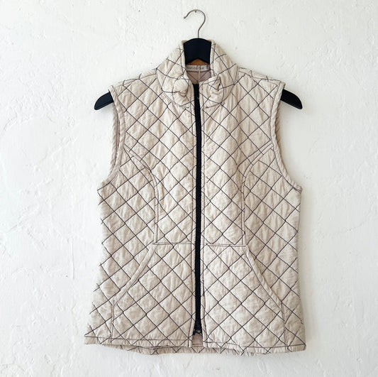 Cream-colored quilted vest with a diamond pattern on a hanger against a white wall