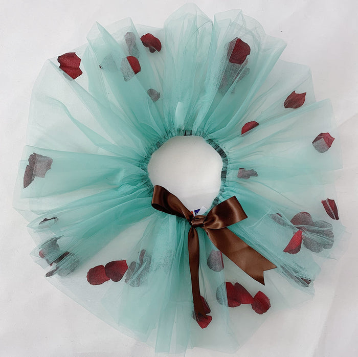 A green tutu with an elastic waistband and a brown bow in the front, decorated with red and dark red petal accents spread throughout.