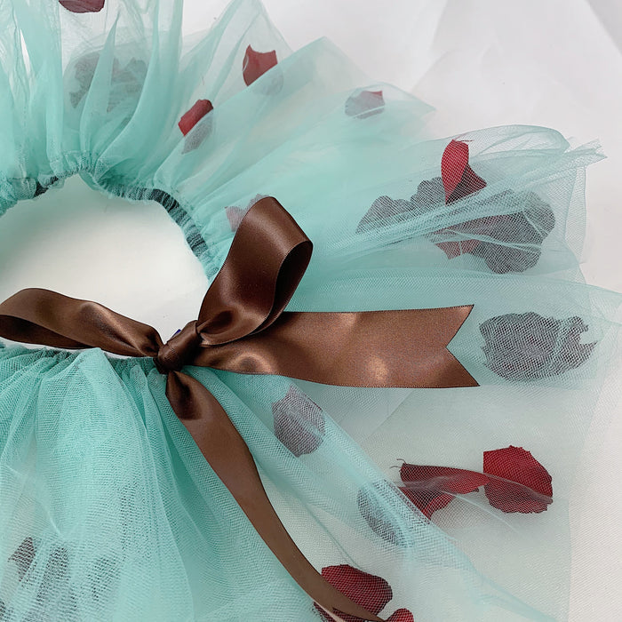 Close-up of the brown bow of the green mesh material of the tutu and dark red petals