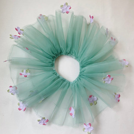 A sage green tutu with lavender colored flowers and an elastic waistband, displayed on a neutral background.