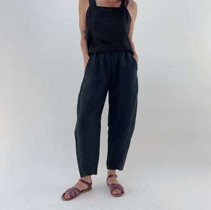 Person with their hands in their pockets wearing black linen pants and a black linen tank on a white background.