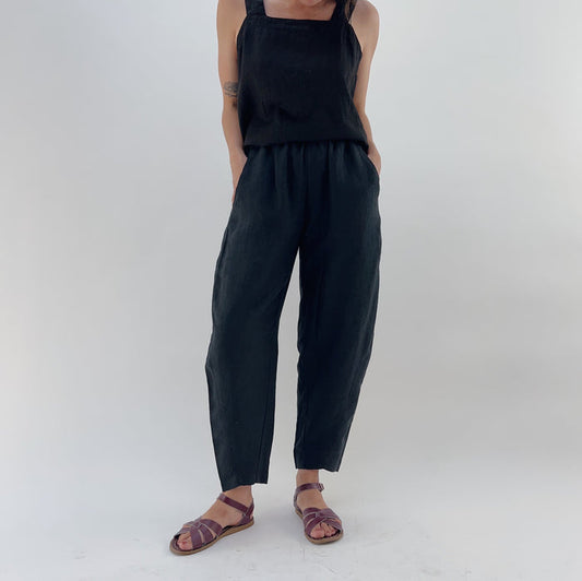 Person with their hands in their pockets wearing black linen pants and a black linen tank on a white background.