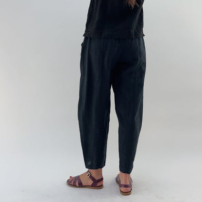 Person wearing black linen pants and a black linen tank on a white background as seen from behind.