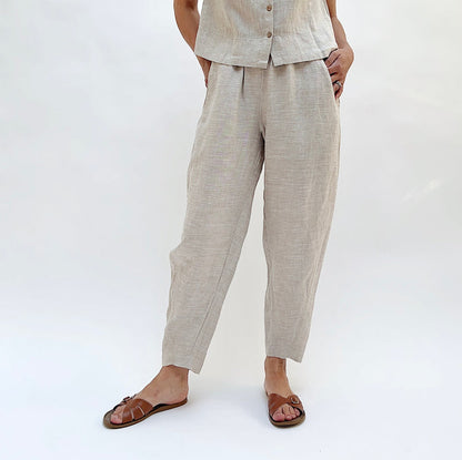 Person with their hands in their pockets wearing beige linen pants and a matching top on a white background.