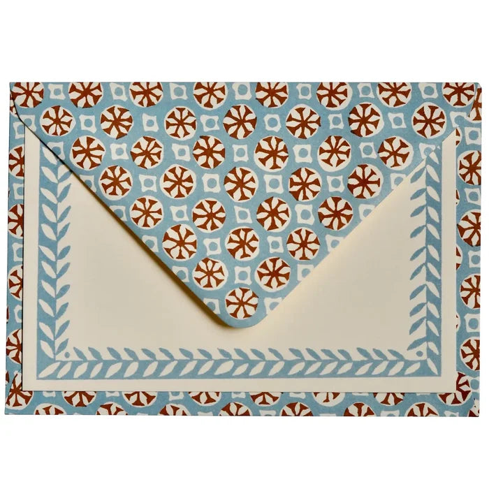 A square envelope with a cream-colored interior and a light blue border decorated with a leaf pattern, set against a matching patterned background. The patterned background features repeating brown and white floral medallions on a light blue base.