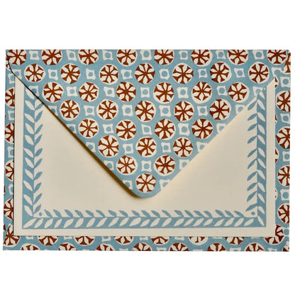 A square envelope with a cream-colored interior and a light blue border decorated with a leaf pattern, set against a matching patterned background. The patterned background features repeating brown and white floral medallions on a light blue base.