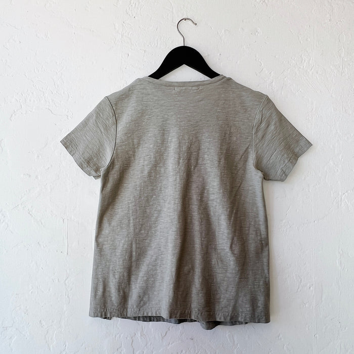 Green t-shirt on a hanger against a white wall, viewed from behind