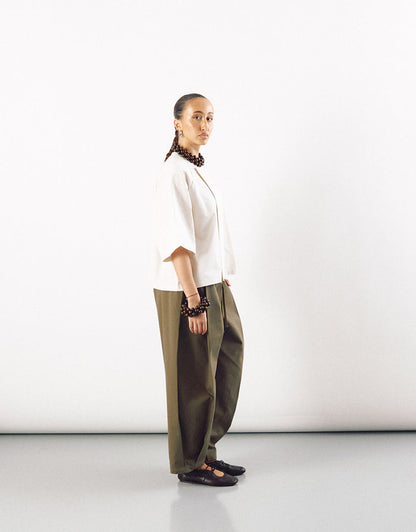 Side view of a model wearing an off-white short sleeve minimalist shirt paired with wide-leg olive green pants, styled with dark accessories and black shoes.