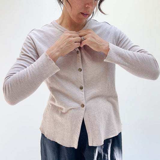 A person wearing a beige crop cardigan with long sleeves, snap buttoned front, and a round neckline.