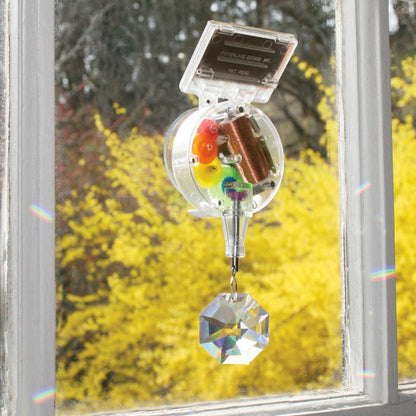 A solar-powered rainbow maker attached to a window, consisting of a solar panel and a hanging crystal.