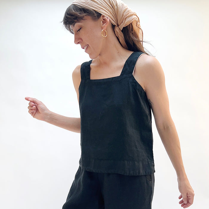 Woman wearing a black sleeveless top and beige headscarf on a white background
