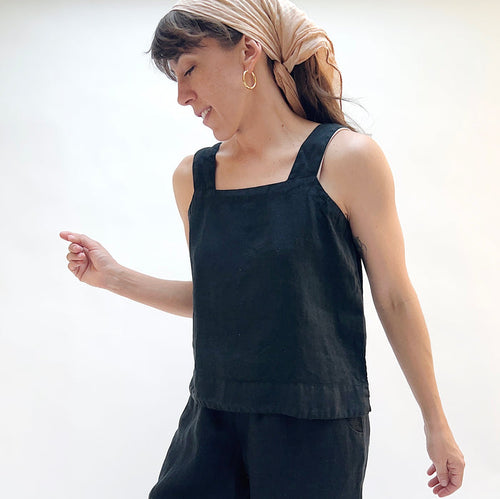 Woman wearing a black sleeveless top and beige headscarf on a white background