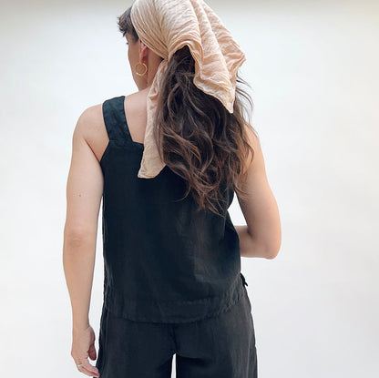 Person wearing a black sleeveless top and beige headscarf on a plain background, viewed from the back