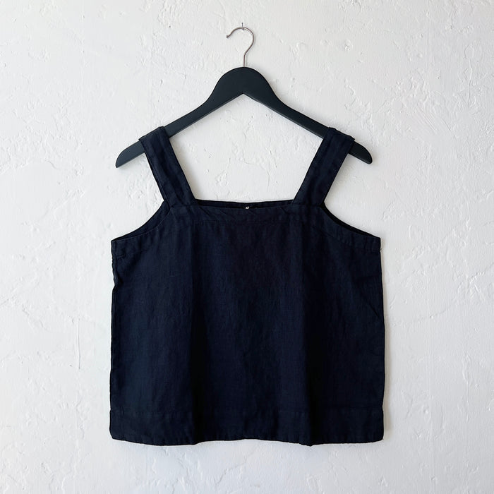 A square neck linen tank in black, hanging on a hanger against a white wall.