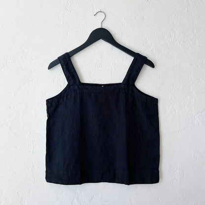A square neck linen tank in black, hanging on a hanger against a white wall.