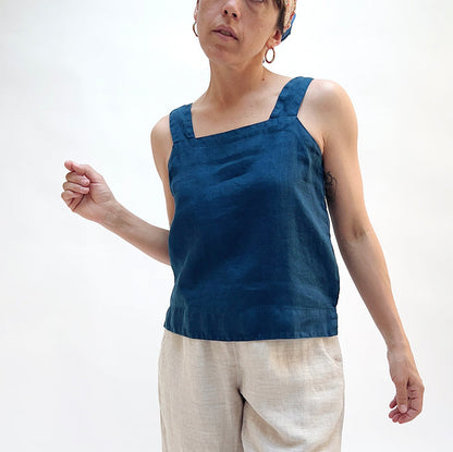 Person wearing a blue sleeveless top and beige pants on a white background