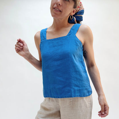 Person wearing a blue tank top and beige pants against a white background