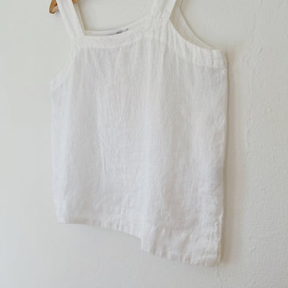 White tank top hanging on a wooden hanger against a white wall.