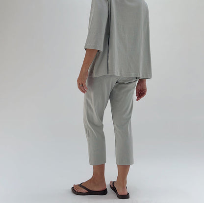 Three-quarter back view of model wearing Pacific Cotton orlaya Sunday pant, showing elastic waistband, relaxed fit through hip, cropped tapered leg, and sage green color