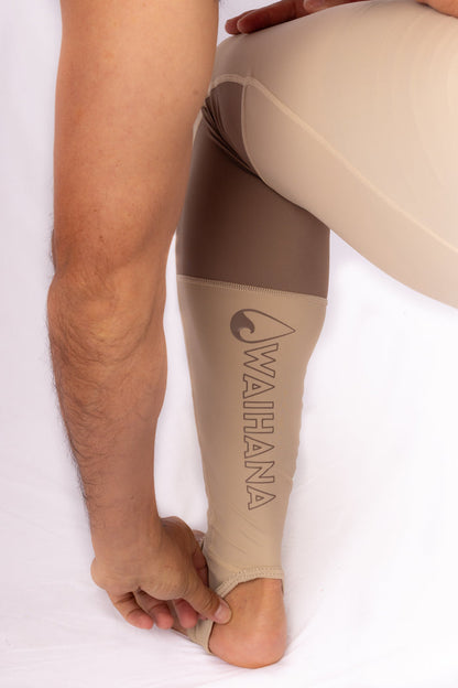 Man wearing Waihana Tan Carvico Lycra leggings with a brown and tan color-block pattern and Waihana logo printed on the lower leg, shown against a white studio background.